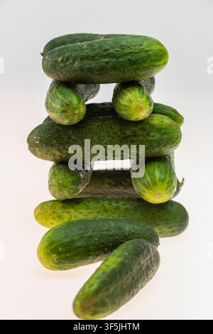 Kreative konzeptionelle Studio-Stillleben von ganzen Gurken, die vertikal in einem ausgewogenen Turm gestapelt sind, auf weißem Hintergrund. Die verspielte Stapelungsanordnung Stockfoto