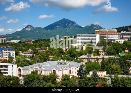 Eine Tagespanoramik einer Stadt, die sich zwischen üppigen grünen Bäumen erstreckt, mit einer markanten Bergkette im Hintergrund. Die städtische Landschaft zeigt eine Mi Stockfoto