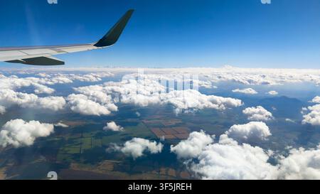 Eine Luftaufnahme aus einem Flugzeugfenster während eines Tagesflugs. Die linke Seite des Bildes zeigt einen Teil des weißen Flugzeugflügels. Unten, verstreut Stockfoto