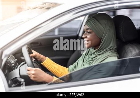 Fröhliche Afrikanische Muslimische Dame Im Kopftuch Auto Fahren In Der Stadt, Seitenansicht Stockfoto