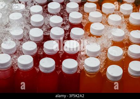 Plastikflaschen mit Rosellen-Saft und Orangensaft, gekühlt in zerkleinertem Eis auf einem thailändischen Straßenmarkt für ein erfrischendes Getränke-Menü. Stockfoto