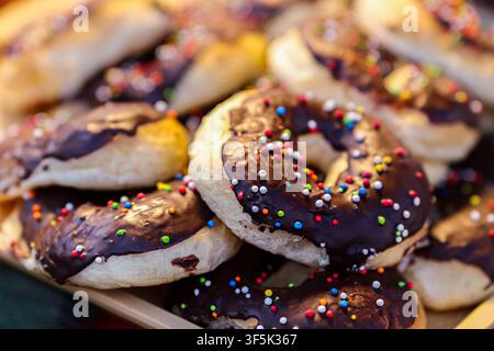 Schokoladenüberzogene Donuts mit bunten Regenbogenstreuseln, gestapelt auf einem Backwarentablett, Nahaufnahme. Stockfoto
