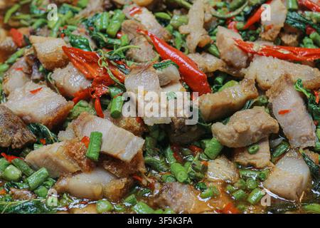 Nahaufnahme von thailändisch gebratenem knusprigem Schweinebauch mit heiligem Basilikum, roter Chili und langen Bohnen, die mit einer glänzenden braunen Soße überzogen sind. Stockfoto
