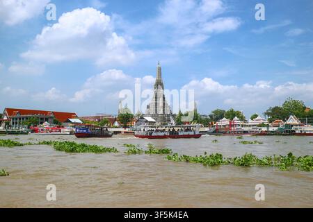Passagierboote kreuzen den Chao-Phraya-Fluss vor dem Wat Arun Tempel in Bangkok, Thailand, unter einem blauen Himmel mit Wolken. Stockfoto