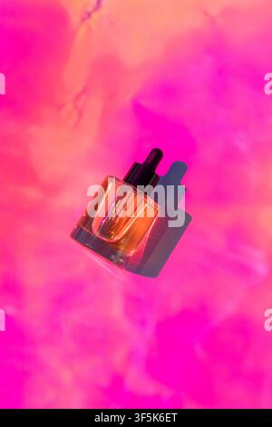 Glas-Tropfflasche mit kosmetischem Gesichtsserum auf einem lebhaften rosa und korallenfarbenen Hintergrund, mit dramatischem Schatten und leuchtenden Farben für die Hautpflege, Feuchtigkeit Stockfoto