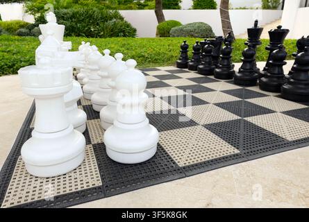 Gigantisches Schachspiel im Freien, weiße und schwarze Figuren auf dem Brett im Hotelgarten für Aktivitäten im Freien. Stockfoto