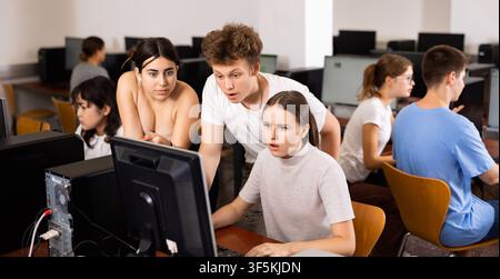 Zielgerichtete Teenager helfen der weiblichen Klassenkameradin, während sie in der Klasse Computerwissenschaften erlernt Stockfoto