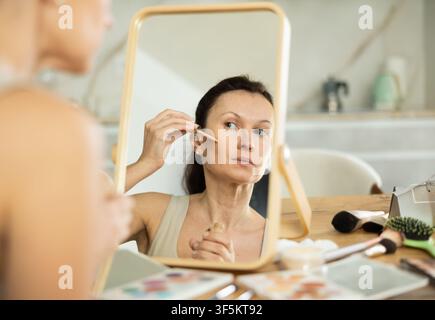 Frau mittleren Alters, die flüssige Foundation auf ihr Gesicht aufträgt Stockfoto