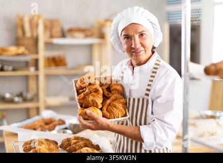 Porträt einer alten Bäckerin, die im Backhaus arbeitet, Tablett mit frischem Backwaren in der Küche hält Stockfoto