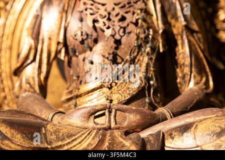 Nahaufnahme einer goldenen Buddha-Statue mit detaillierten Händen in Meditationsmudra, die Frieden, Spiritualität und Erleuchtung mit kompliziertem ornamentalem Design symbolisieren. Stockfoto