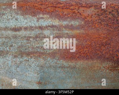 Makroaufnahme einer korrodierten Metalloberfläche, die reiche orange-braune Rostflecken zeigt, die sich mit verblassten stahlblauen Tönen vermischen. Stockfoto