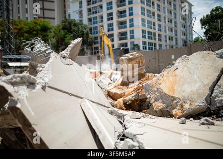 Bruchstücke von Betonplatten mit Bewehrung im Nahaufnahme mit Bagger, der im Hintergrund einen hydraulischen Brecher verwendet, auf einer Abrissbaustelle Stockfoto