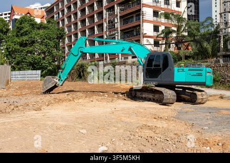 Türkis-Bagger mit Schaufel, der Erde auf einer Baustelle in der Nähe eines Wohnhauses ausgräbt Stockfoto