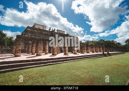 Alter Tempel erhebt sich unter strahlend blauem Himmel. Wolken ziehen über Steinsäulen und Stufen. Grünes Gras bedeckt die Basis des Tempels. Sonnenlicht hebt abgenutzte Stockfoto