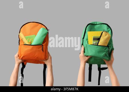 Zwei Hände halten bunte Schulrucksäcke, die mit Bildungsutensilien für die Rück-zur-Schule-Saison gefüllt sind, zwei Hände halten einen orangefarbenen Rucksack und ein Stockfoto
