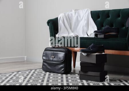 Herrenformkleidung mit weißem Hemd, schwarzem Aktendkoffer und blauen Wildlederschuhen auf einem grünen Samtsofa und Schuhschachteln Stockfoto