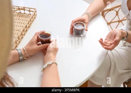 Zwei Frauenhände, die Kaffeetassen auf einem weißen Tisch halten, Konzept für lockere Gespräche und soziale Zusammenkünfte, die Szene deutet auf ein lockeres Gespräch oder s Stockfoto