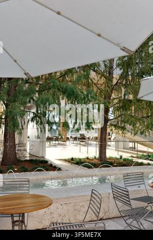 Zypressen rahmen einen Innenhof-Spiegelpool im Getty Center ein, gesehen von der Caféterrasse unter einem großen Schirm, Los Angeles Stockfoto