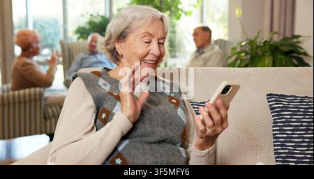 Seniorin, winkende und glückliche Frau mit Telefon für Videoanruf, Gespräch oder Begrüßung im Seniorenheim. Ältere, weibliche Person oder Lächeln mit Smartphone Stockfoto