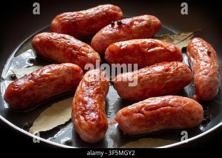 Gebratene Fleischwurst in einer Pfanne, Nahaufnahme. Frische Würste mit Paprika und Lorbeerblättern. Stockfoto