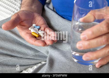 Nahaufnahme eines älteren Mannes, der sitzt und verschiedene Pillen in der Hand hält, während er ein Glas Wasser hält. Konzept der täglichen Medikation, Gesundheitsvorsorge-Routine Stockfoto