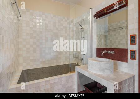 Zeitgenössisches Badezimmerinterieur mit großer eingebauter Badewanne, gefliestem Umfeld, modernem Waschtischspiegel, Arbeitsplattenspüle, neutralen Tönen, hell Stockfoto