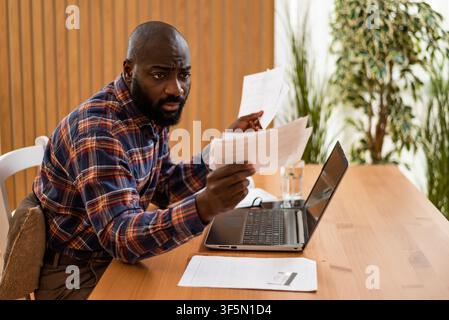 Von Papierkram überwältigt, kämpft ein Mann, um seine Finanzen zu organisieren, während er von zu Hause aus arbeitet. Stockfoto