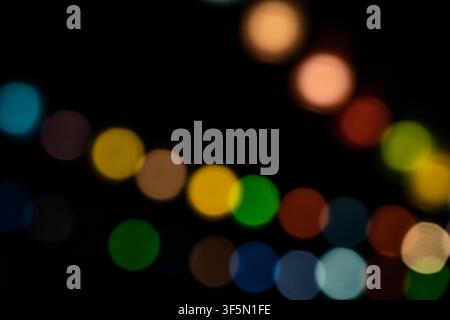 Farbenfroher Bokeh-Lichterhintergrund, abstrakte unscharfe Kreise in gebogener Linie auf dunklem Hintergrund, festliche Nachtextur Stockfoto