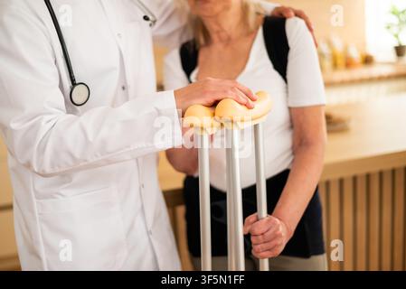 Close Up of Doctor bietet eine beruhigende und körperliche Unterstützung für eine ältere Patientin, die Unterarmkrücken zu Hause verwendet. Stockfoto