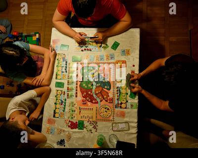 Familie und Freunde spielen ein farbenfrohes Brettspiel zusammen während eines gemütlichen Spielabends zu Hause Stockfoto