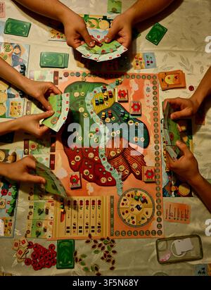 Freunde spielen zusammen ein farbenfrohes Strategiespiel am Tisch mit Karten und Spielsteinen Stockfoto