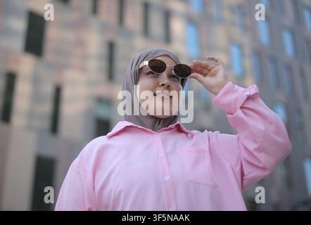 Junge Frau mit Hijab schaut lächelnd in der Stadt nach oben Stockfoto