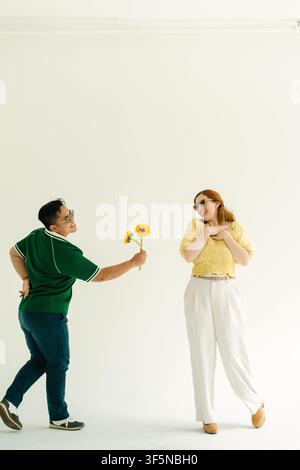 Mann gibt spielerisch Sonnenblumen an eine überraschte Frau Stockfoto
