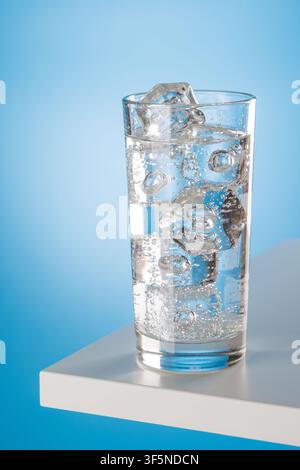 Glas Sprudelwasser mit Eiswürfeln auf weißem Sockel vor blauem Hintergrund, Konzept für frisches Getränk Stockfoto