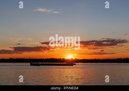 Heller goldener Sonnenuntergang über einem breiten Fluss mit dramatischen Wolken und warmem Abendlicht. Stockfoto