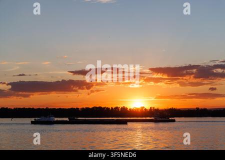 Heller goldener Sonnenuntergang über einem breiten Fluss mit dramatischen Wolken und warmem Abendlicht. Stockfoto