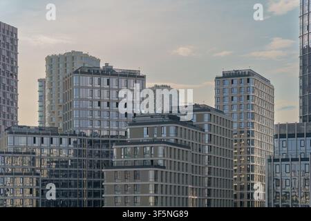 Mehrgeschossige Wohnblöcke mit zeitgenössischen Glasfassaden in einem dichten Stadtviertel. Wohnkomplex aus Wohnhäusern unterschiedlicher Höhen unter bewölktem Himmel Stockfoto