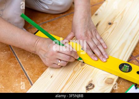 Hände markieren Maße auf einer Holzplatte mit Bleistift und Wasserwaage. Konzept der sorgfältigen Planung hinter jedem Schritt eines DIY-Baus. Stockfoto