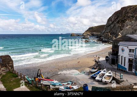 St Agnes an der Küste von Cornwall zeigt einen sandigen und kiesigen Strand mit kleinen Booten, die in der Nähe eines Strandcafés heraufgezogen sind. Felsenformationen umrahmen die Küstenlinie Stockfoto