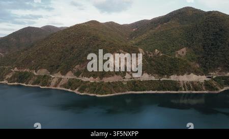 Hohe Luftaufnahme eines Drohnenbildes des Zhinvali-Stausees mit Asphaltstraße entlang der Berghangwälder in der Region Georgien-Kaukasus für Reise-Stock Stockfoto