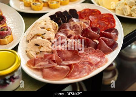Ein großes weißes Tablett zeigt eine Auswahl an Charcuterie, darunter verschiedene Arten von dünn geschnittenen Schinkensorten wie Prosciutto, Salami und Chorizo Stockfoto