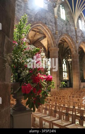 Vase mit Blumen und leere Stühle bei Licht durch das Fenster, ein friedlicher Moment in der St. Giles' Kathedrale, Edinburgh, UK, am 17. Mai 2026. Stockfoto