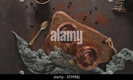 Eine Aufsichtsansicht von zwei einzelnen Tiramisu-Gläsern, die auf einem Holzbrett mit Kaffeebohnen und Löffeln angeordnet sind, beleuchtet von dramatischer, stimmungsvoller Beleuchtung auf Stockfoto