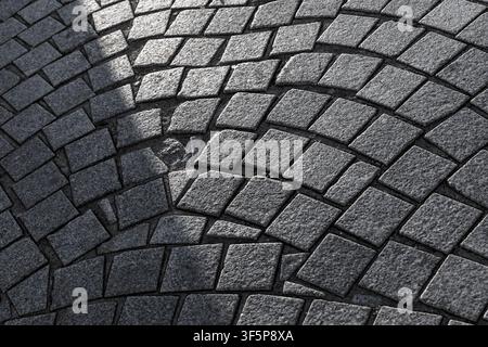 Gekrümmtes Kopfsteinpflaster bildet sich wiederholende bogenförmige Muster, betont durch dramatische Seitenbeleuchtung und tiefe Schatten, die die raue Steinstruktur hervorheben, ge Stockfoto