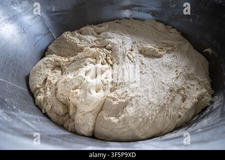 Frischer Rohteig steigt in einer großen industriellen Metallrührschüssel in einer professionellen Backstube, die Textur der Hefebrotzubereitung zum Backen Stockfoto