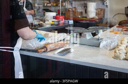 Female baker bereitet rohen Teig vor, schneidet Stücke. Rohe Brotteigportionen auf einem Tisch in einer gewerblichen Bäckerei. Lebensmittelproduktionsprozess und -einrichtung. Stockfoto