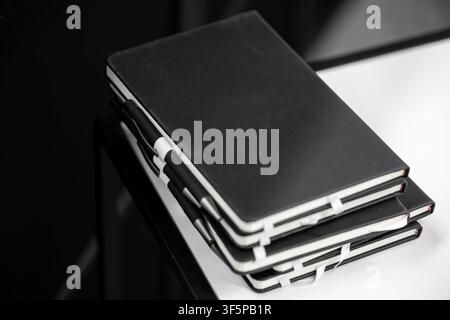 Stapel schwarzer Tagebücher mit Stiften auf einem modernen Schreibtisch Stockfoto