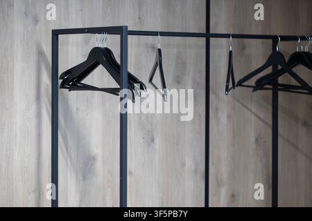 Leere schwarze Kleiderbügel auf einem minimalistischen Metallregal stehen vor einer modernen hellen holztexturierten Wand in einem organisierten Boutique-Ausstellungsbereich, bereit Stockfoto