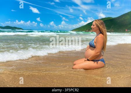 Neun Monate schwangere Frau im dritten Trimester meditiert und entspannt sich an einem tropischen Meeresstrand. Gesunder pränataler Lebensstil, Reisen im Sommerurlaub Stockfoto