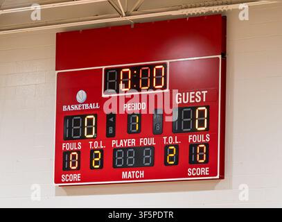 Rotes Basketball-Scoreboard hängt an einer Wand. Digitale Anzeigen zeigen Zeit, Spielabschnitt, Punkte und Fouls. Helle rote Farbe kontrastiert mit dem Hintergrund. Spiel Stockfoto